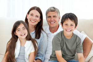 Picture of a family sitting on a sofa smiling. There is a little boy and little girl sitting in their parents laps.